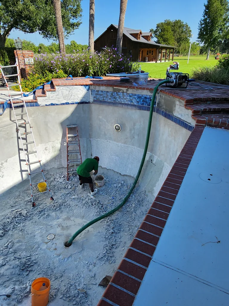 Worker inside a drained pool with demolition debris, ladders and a hose in Bourg, Louisiana