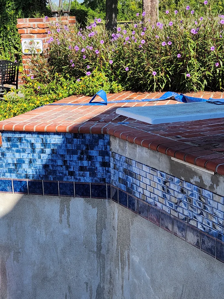 Blue waterline tile installation beneath brick coping during pool renovation in Bourg, Louisiana